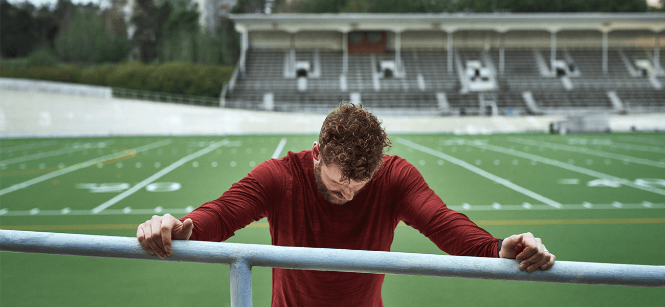“Athlete sitting alone in locker room after training, reflective mood, low light, realistic sports photography, no text, high resolution”